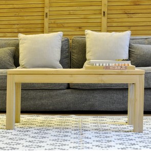 Rechteckiger Massivholz Teak Couchtisch Frankfurt im modernen Design, handgefertigter Sofa Tisch aus der MOEBEL KOLONIE Manufaktur, im Hintergrund Sofa mit in der Farbe dunkel grau Dekoration mit Kissen in der Farbe weiss, Wohnzimmer Moebel nach Mass Muenchen, Accessoire moderner Teppich in Off White mit Boho Muster