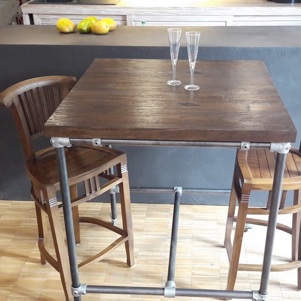 Bar Tisch Amsterdam mit Massivholz Platte aus Teak und Rohrgestell, Industrial Style, Crossover aus Metall und Edelholz Teak massiv, Tisch Platte vom Schreiner Traditionell in Handarbeit gefertigt in der MOEBEL KOLONIE Manufaktur, Massivholz Teak Bar Stuehle Pfau, Dekoration mit den Accesoieres Sekt Floeten, im Hintergrund gelbe Zitronen auf schwarzer Anrichte, Mass Moebel Muenchen