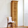 Massiver Teak Schrank Paola mit Massivholz Stuhl Antonio Dekoration ein Handtuch in der Farbe weiss, Massivholz Hochschrank mit einer Schwingtuere in Shutter Optik mit zwei Schubladen im unteren Bereich, Massivholz Moebel nach Mass fuer das Badezimmer, den Flur oder den Wohnbereich fuer ein mediterranes Flair im Ambiente, Mass Moebel ausTeak massiv vom Schreiner traditionell gefertigt, Manufaktur und Design Muenchen